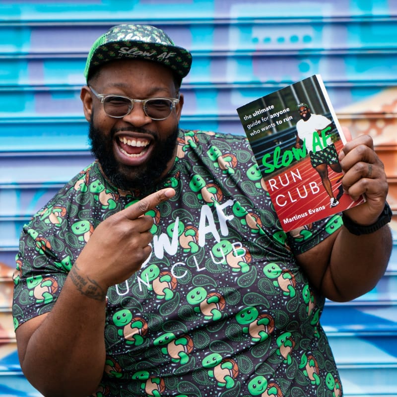 Martinus Evans holds up his book, 'Slow AF Run Club," and points to it.