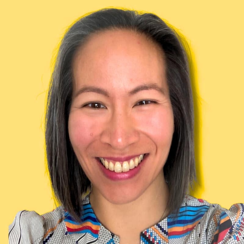 Eagranie Yuh, TEDx Speaker, Writer, and Editor, smiles against a bright yellow background. She is an asian-Canadian woman living in Tasmania, and is a decluttering expert.