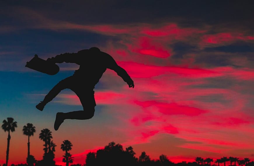 silhouette of person jumping while holding skateboard