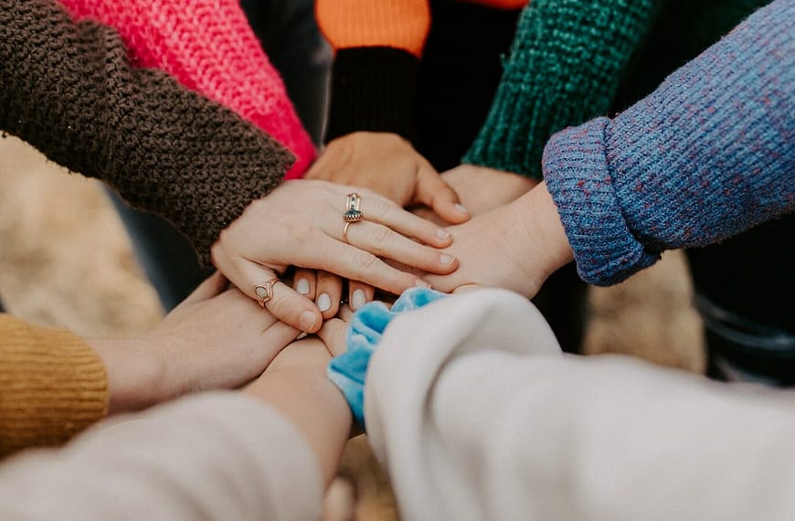 person in red sweater holding babys hand