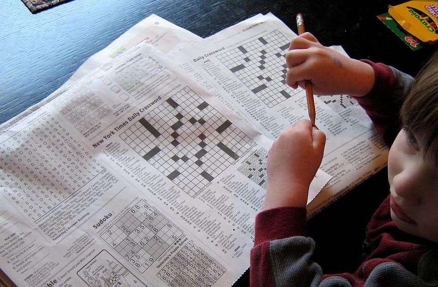 Image: child sitting in front of two crossword puzzles pretending to solve them