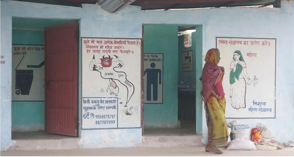 Image: woman walking outside of a SHRI bathroom facility where poo is being turned into a resource
