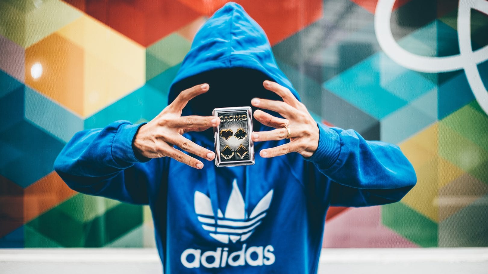 Image: Person in a blue sweatshirt creating the illusion that a deck of cards is hovering between his hands, similar to the tricks of magician David Kwong