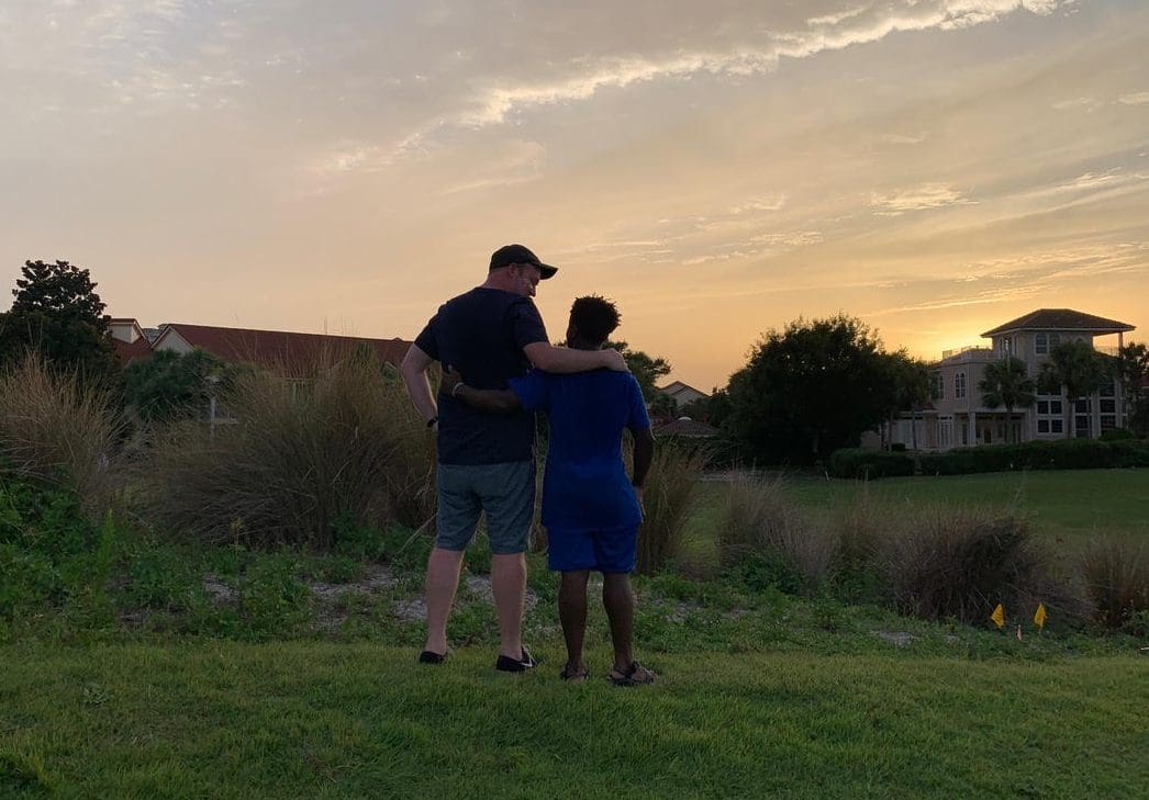 Image: Brad and Robby embracing, with their backs to the camera, watching the sunset