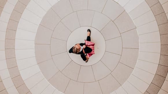 Image: A woman dressed in business casual clothing, walking through a square. The image is taken from directly above.