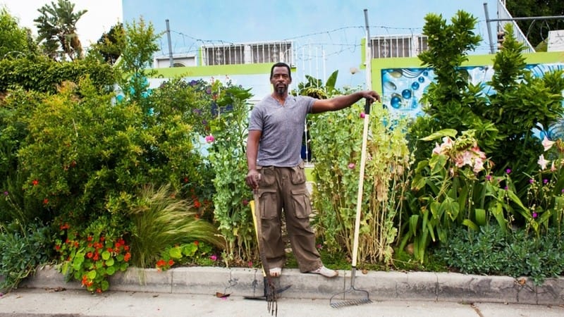 Image: Ron Finley standing on the curb of a street-side garden holding some key gardening essentials