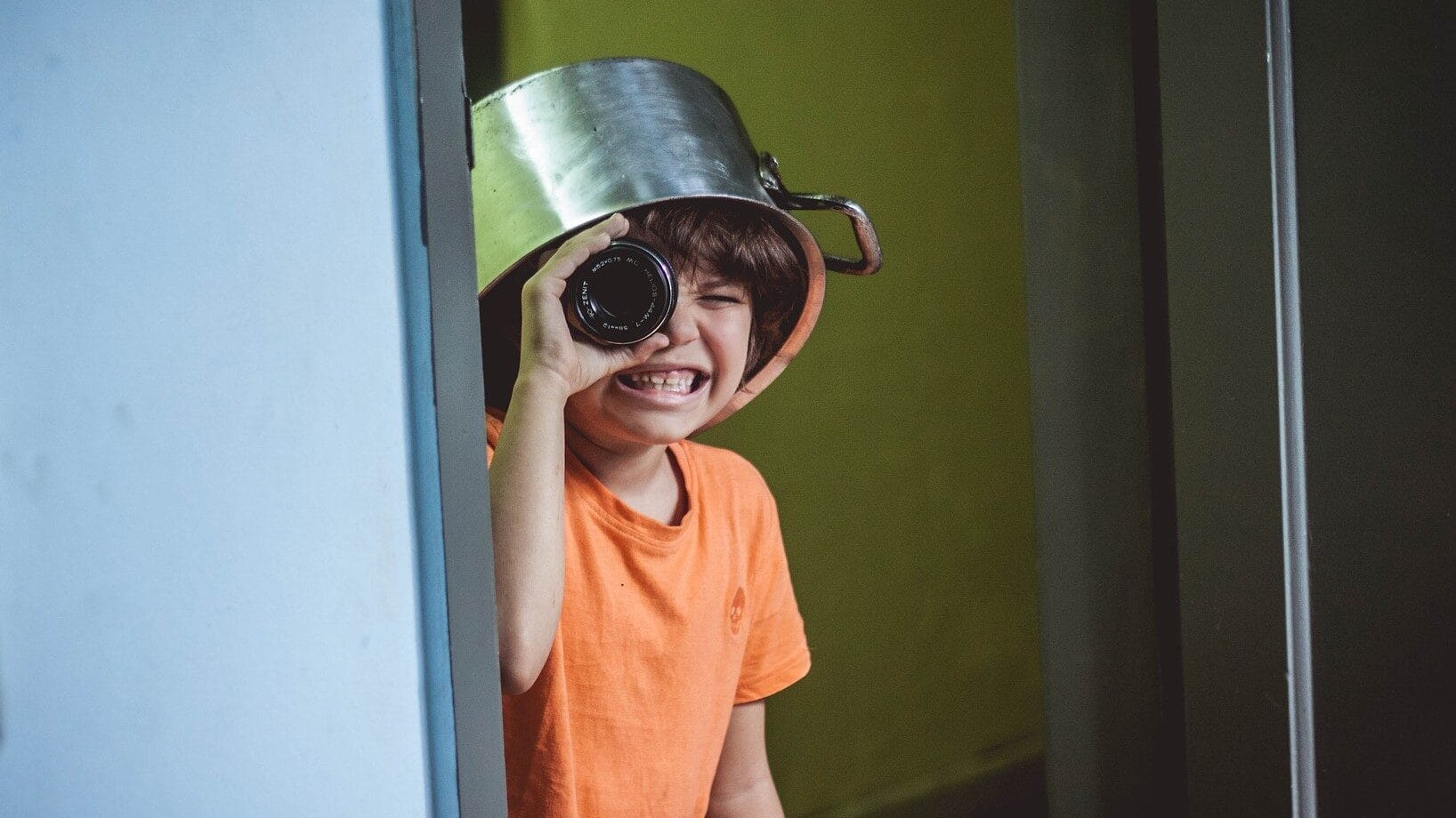 Image: Kids being kids, Kid wearing a kitchen pot on their head, peeking around the corner with a camera lens as a telescope