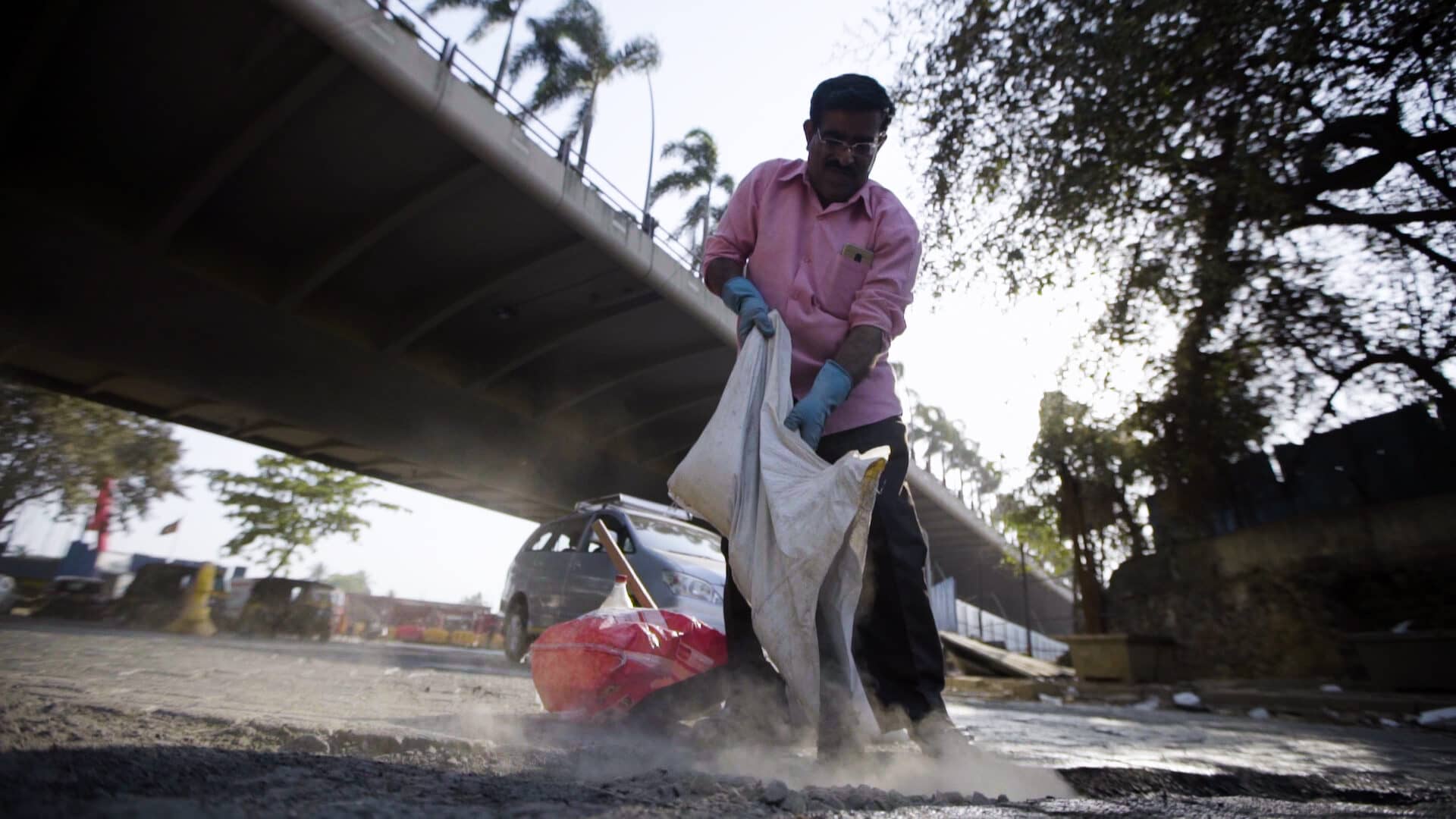 Image: man holding bag, pouring in contents to fill pothole in busy road