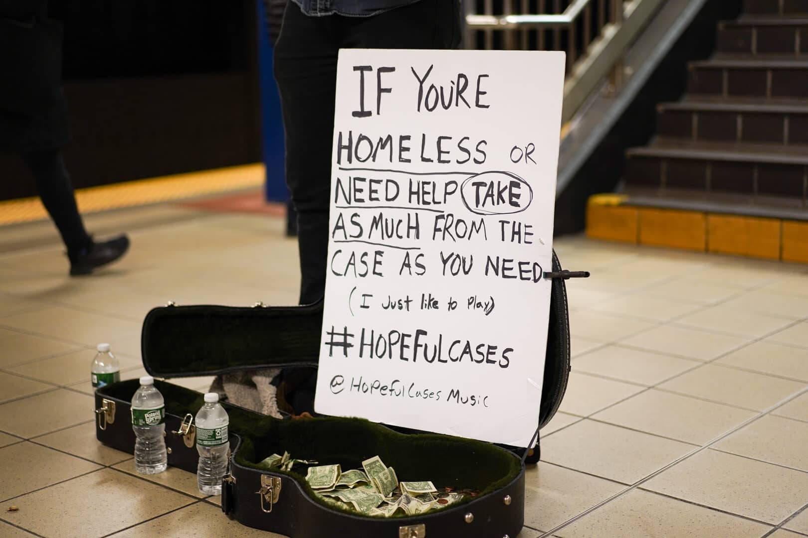 Image: Close up image of the sign Will uses, and his case with money inside. 