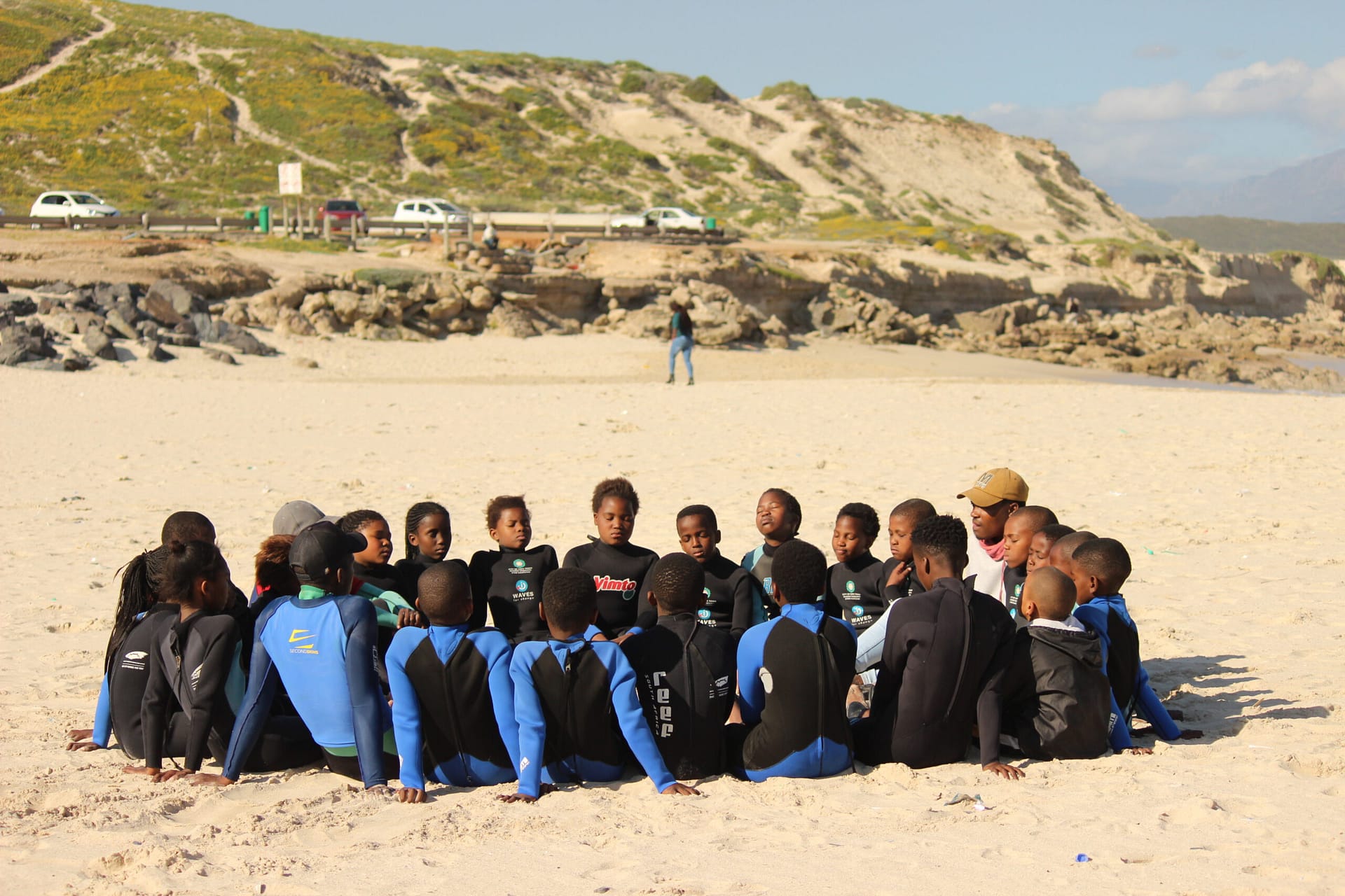 Image: group of children and coaches sitting in a circle with their eyes closed