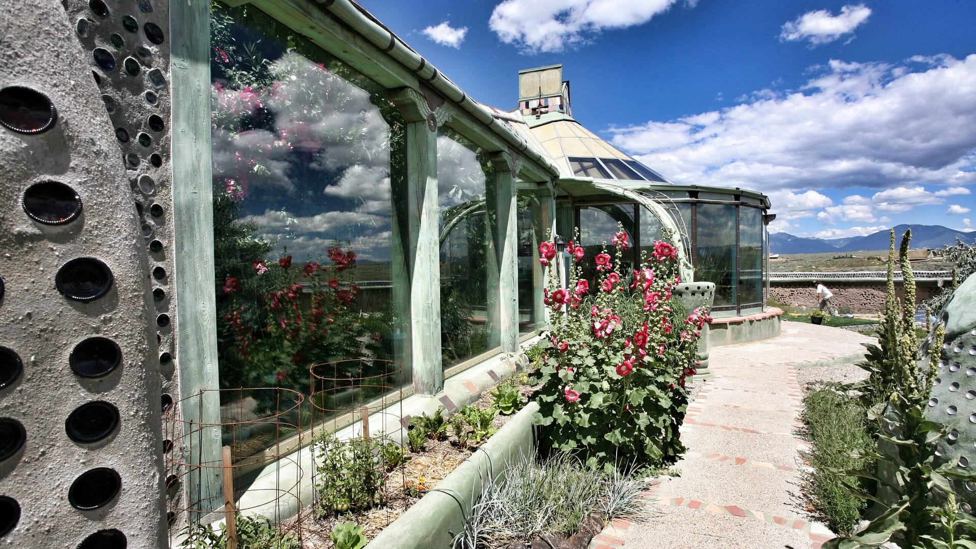 Image: View along the outside wall of an Earthship. Plants are seen growing inside and out!