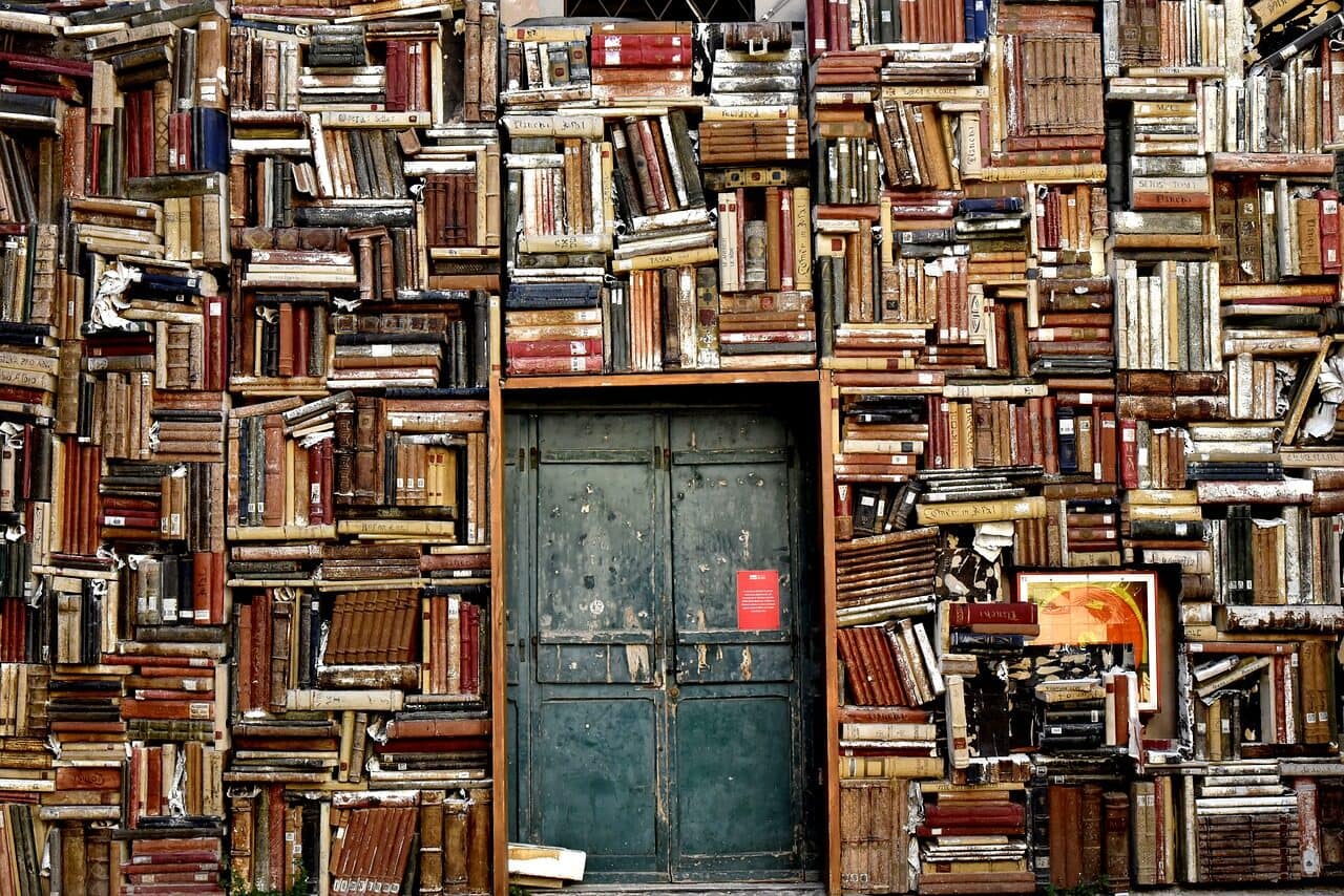 Image: Books stacked along a wall, lining a doorway 