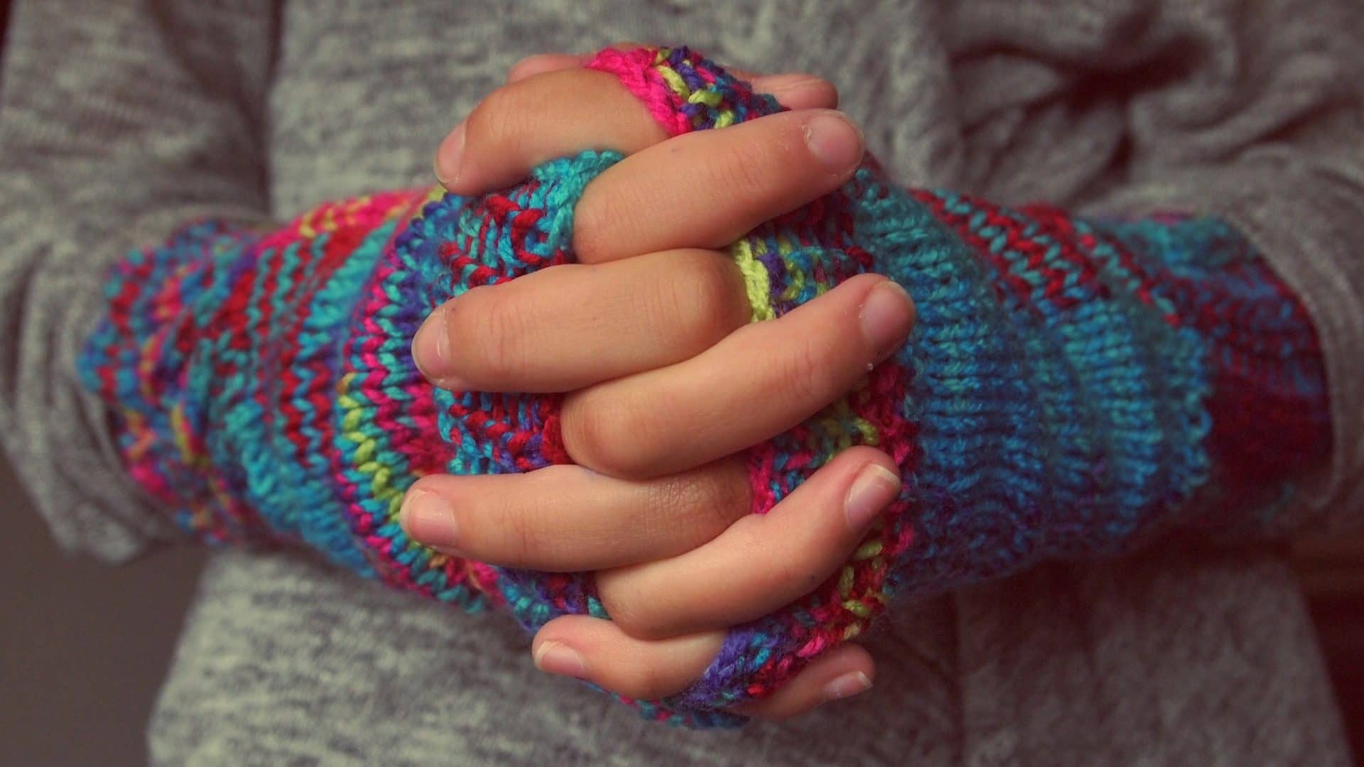 Image: Woven Hands Wearing Knit Gloves like the knitting projects Madame Tricot uses to help heal trauma with patients
