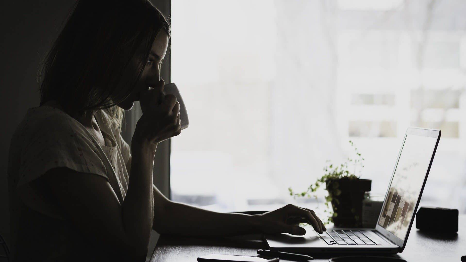 Image: Person drinking coffee and looking intently at their laptop