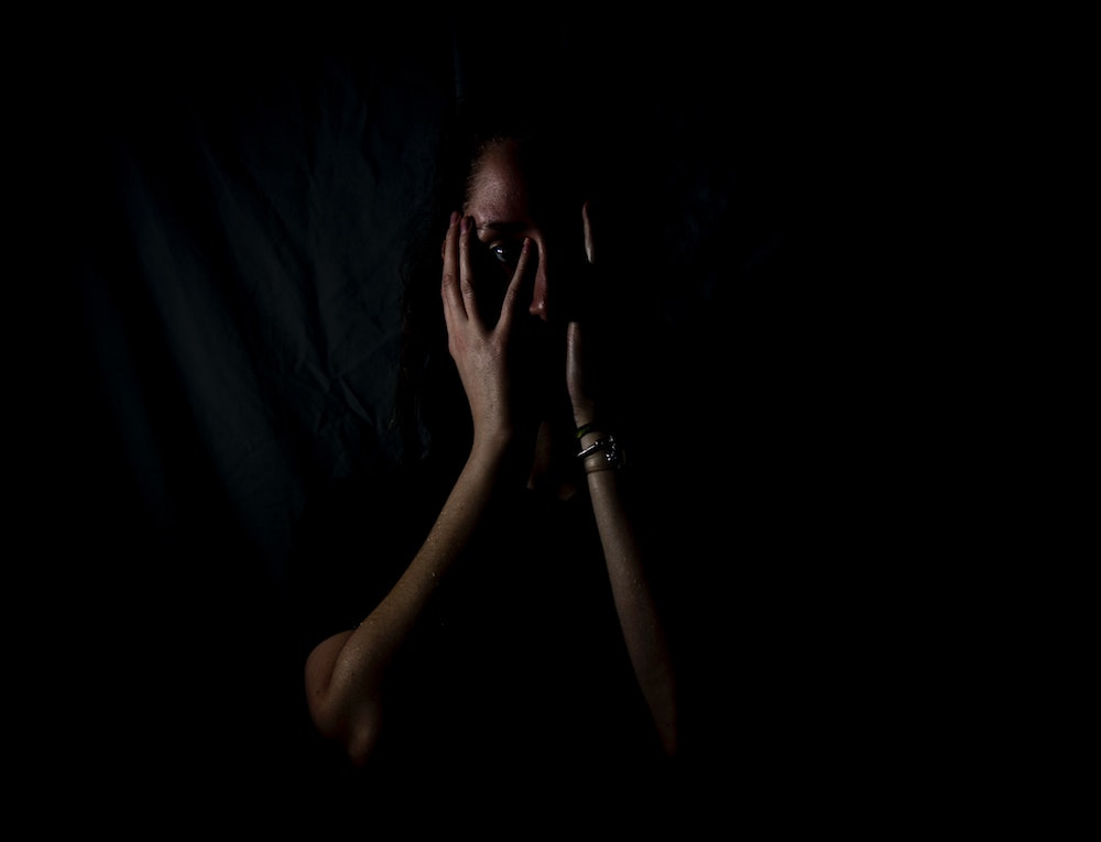 Image: A person in the dark holding their head in their hands