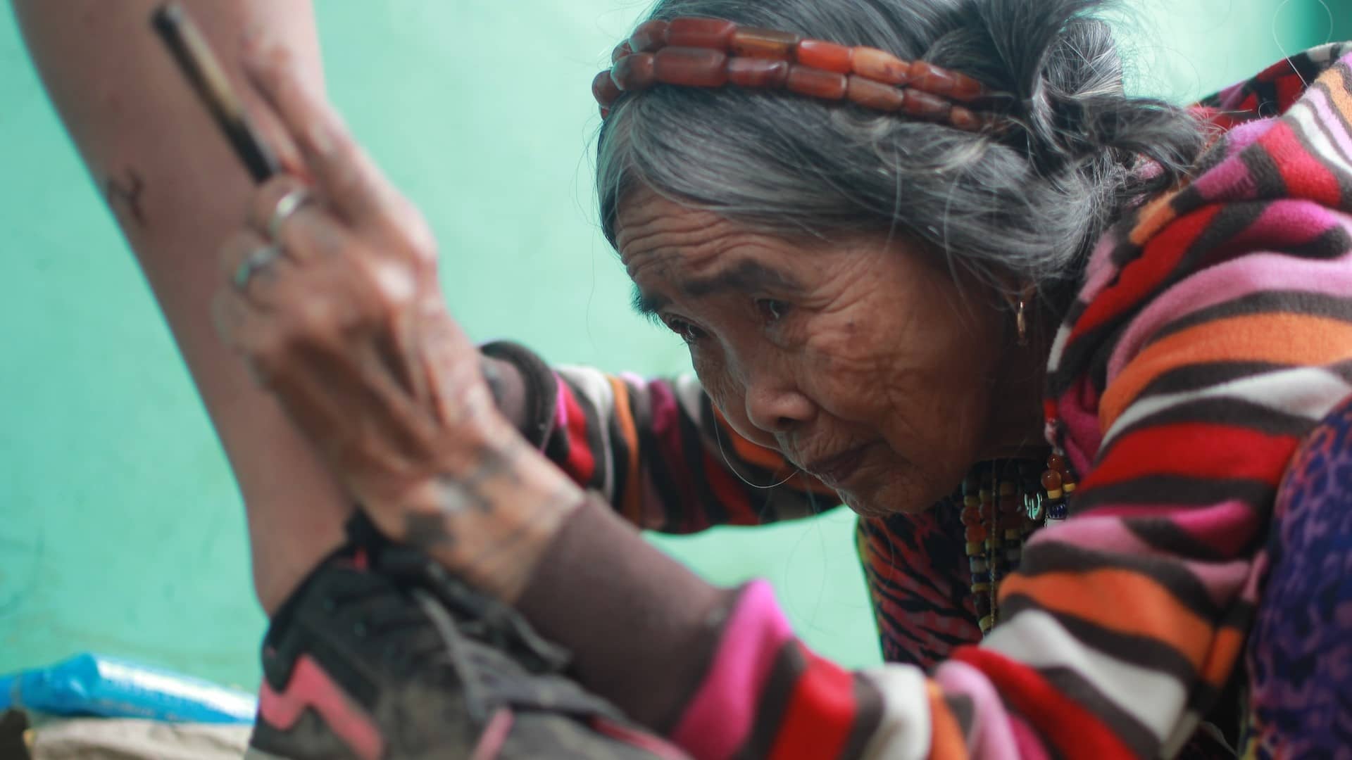 Image: Filipino tattoo artist,106-year-old Apo Whang-Od, tattooing a customer's ankle