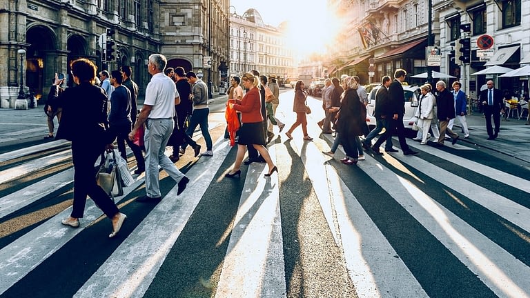 Image: a crowd of people walking across a street backlit by the setting sun