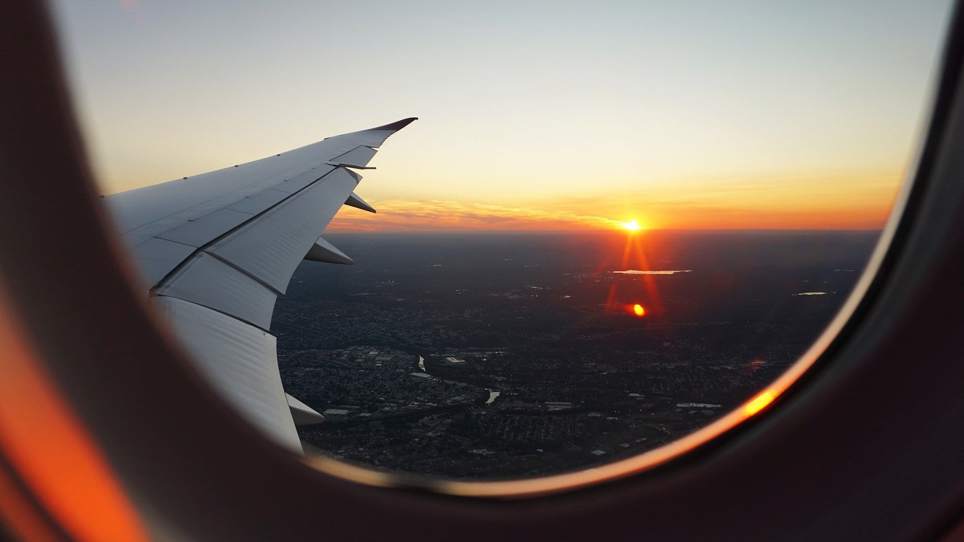 Image: Image taken from inside a plane of a plane wing with a sunset behind it
