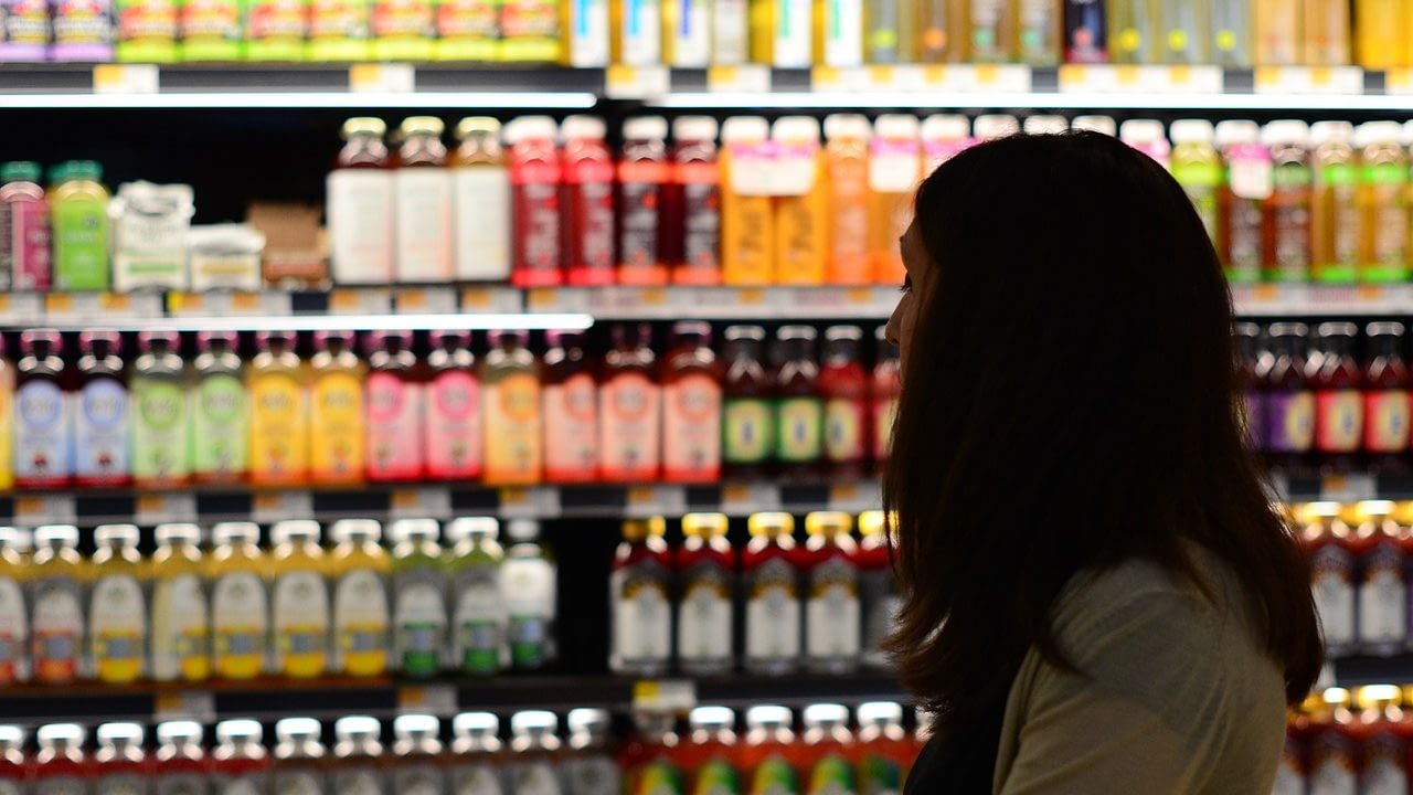 Image: Person grocery shopping. They're next to a wall of bottles.