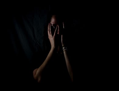 Image: A person in the dark holding their head in their hands