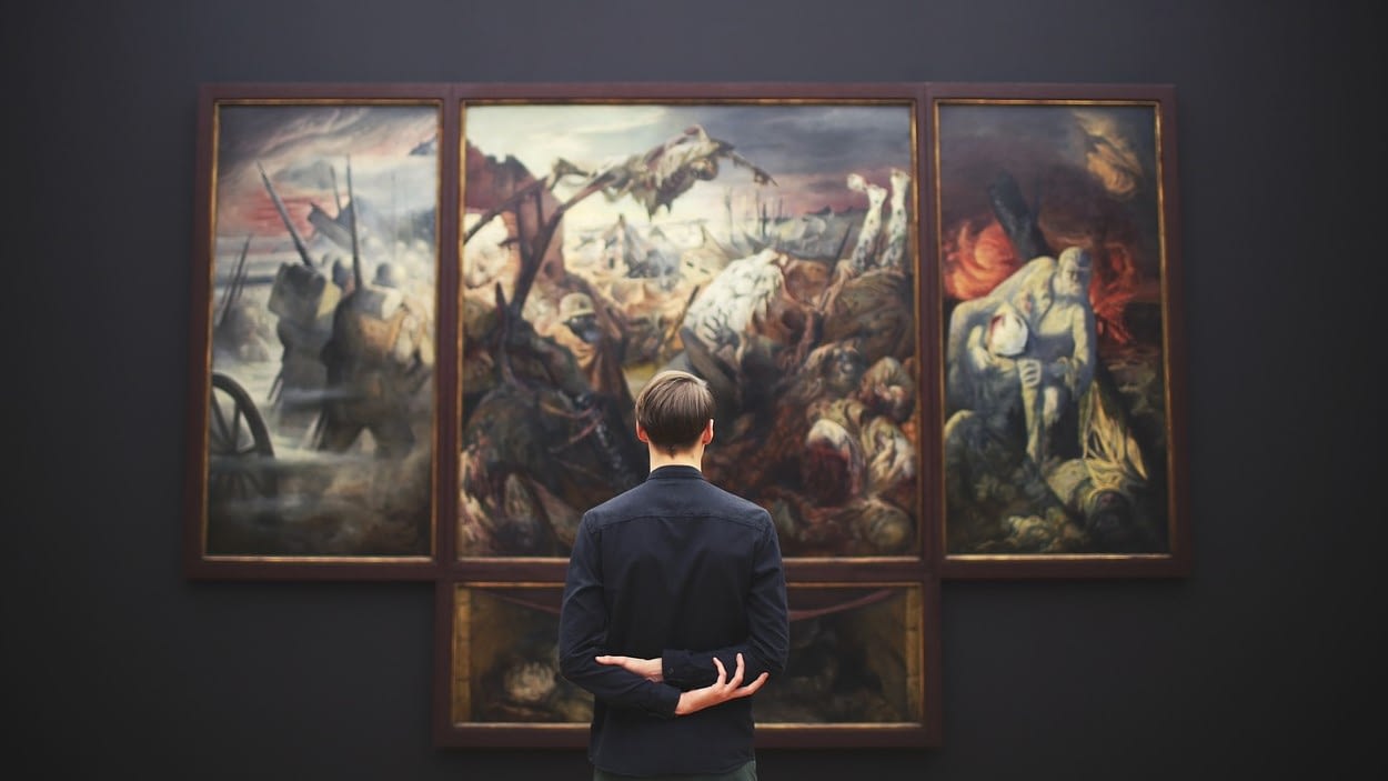 Image: person standing infront of a large painting with their hands behind their back