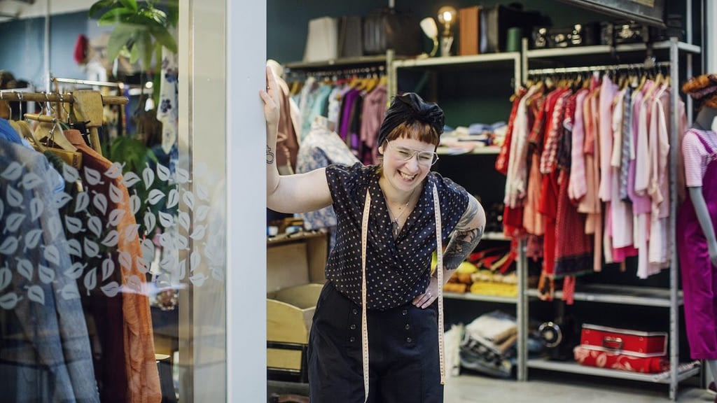 Image: A woman laughing, behind her are recycled clothes in a mall storefront.