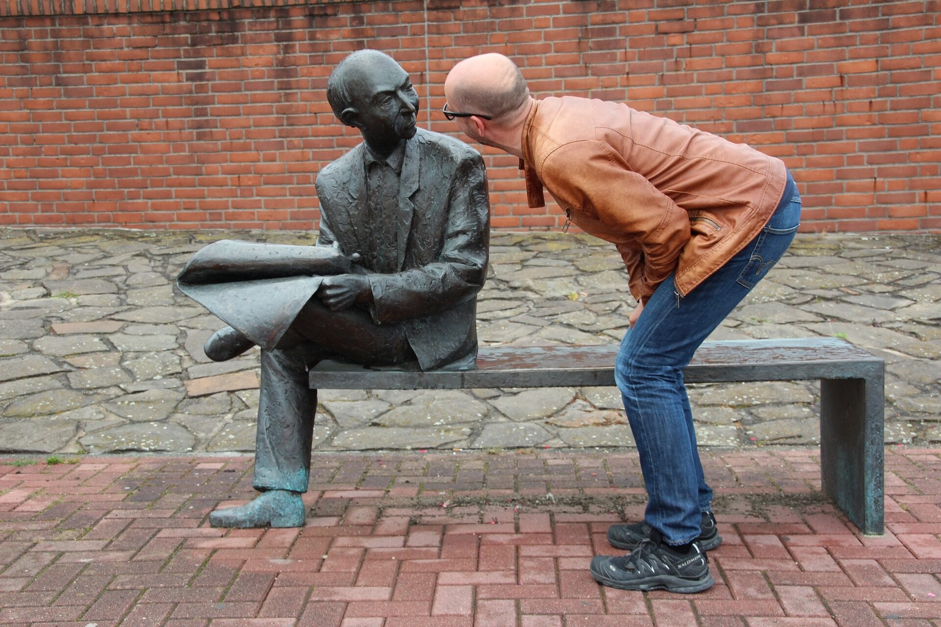 Image: Man pretending to talk to a sculpture of an old man sitting on a bench reading the newspaper