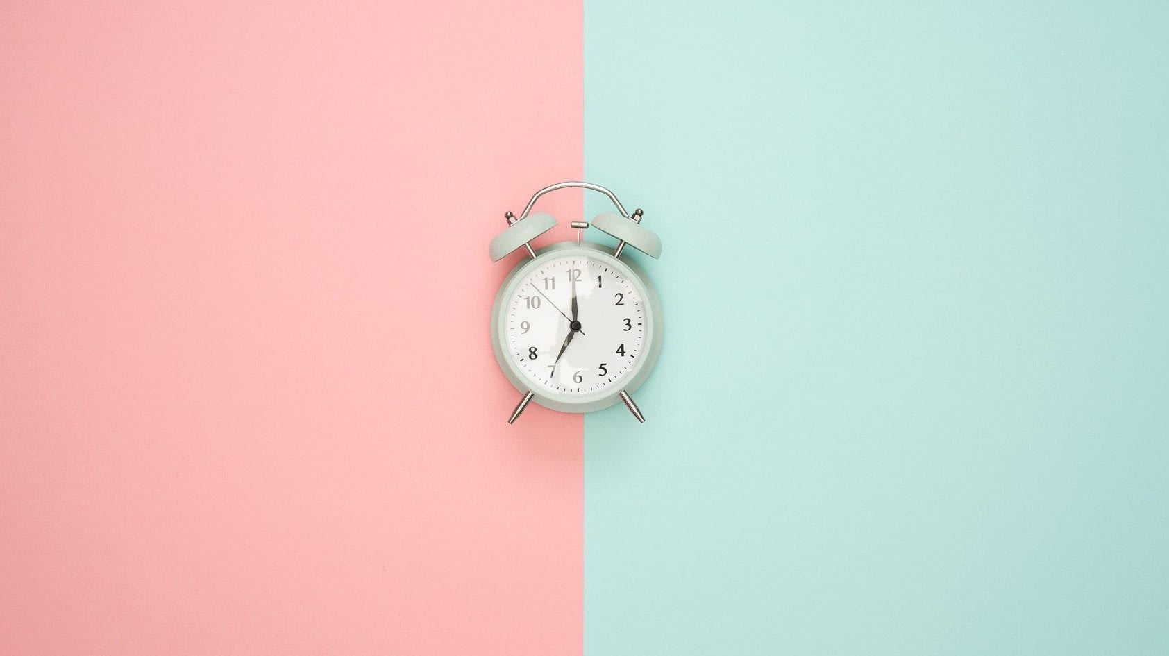 Image: Alarm clock on a background with two different colors splitting the image down the middle representing two ways of seeing time