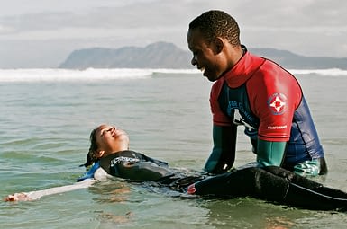 Image: A child smiling and laying on their back in the ocean while a coach lifts them up