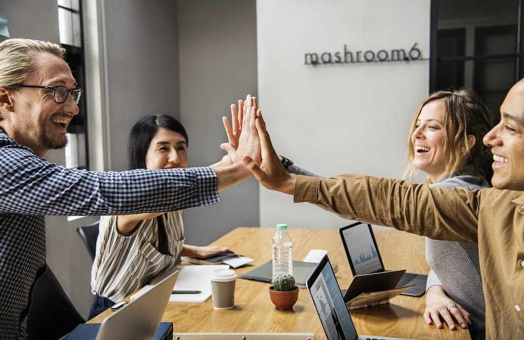 Image: A group of four people high fiving at work, since they've unlocked the happiness advantage.