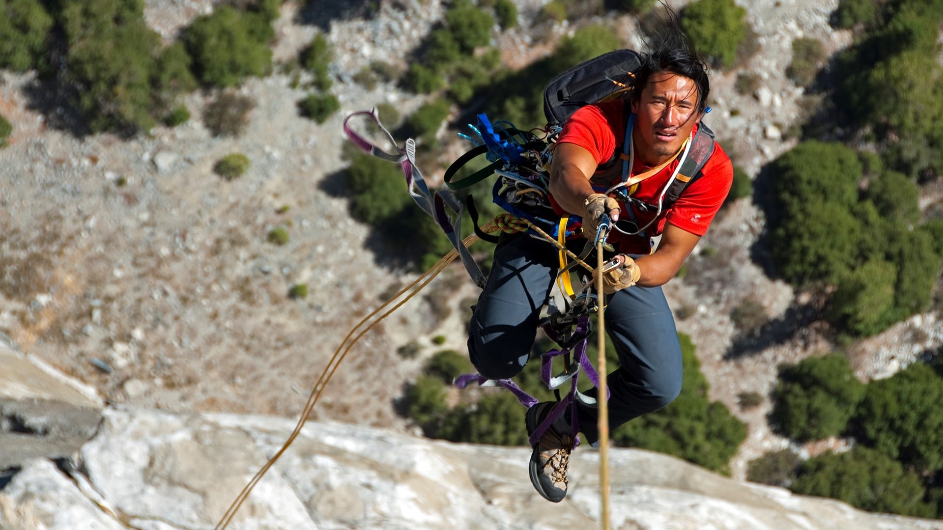 Image: Jimmy Chin hanging from a rope while climbing a mountain.