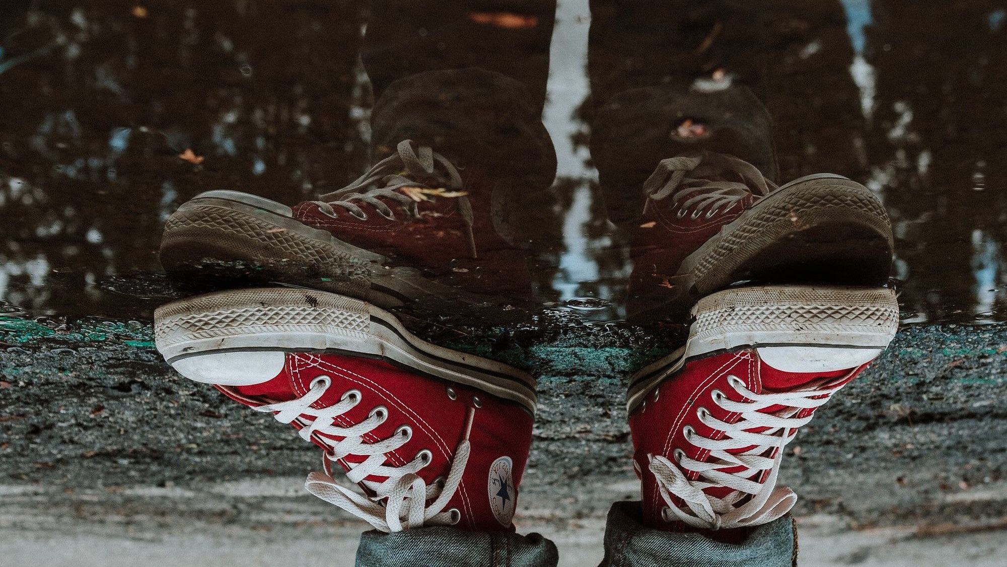 Image: The reflection of red sneakers in a puddle, looking upside down.