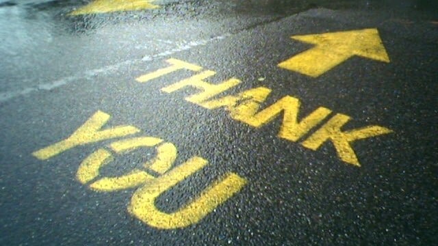 Image: The words Thank You painted on a wet street with an arrow