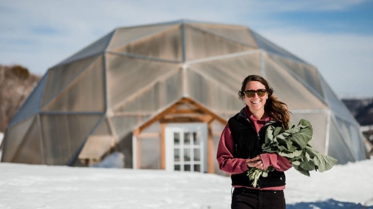 Image: Intern standing outside in the snow with greens from their greenhouse!