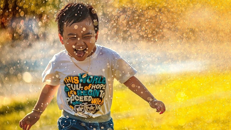 Image: kid smiling and running in sprinklers
