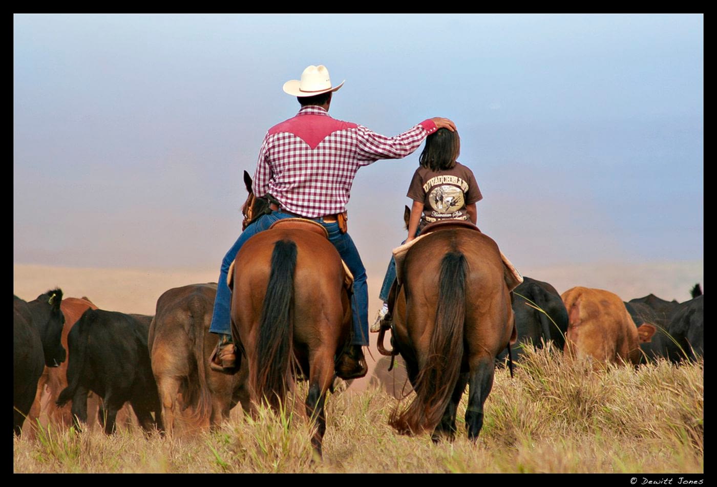 Image: Cowboy puts his hand on a child's head as they ride horses next to each other