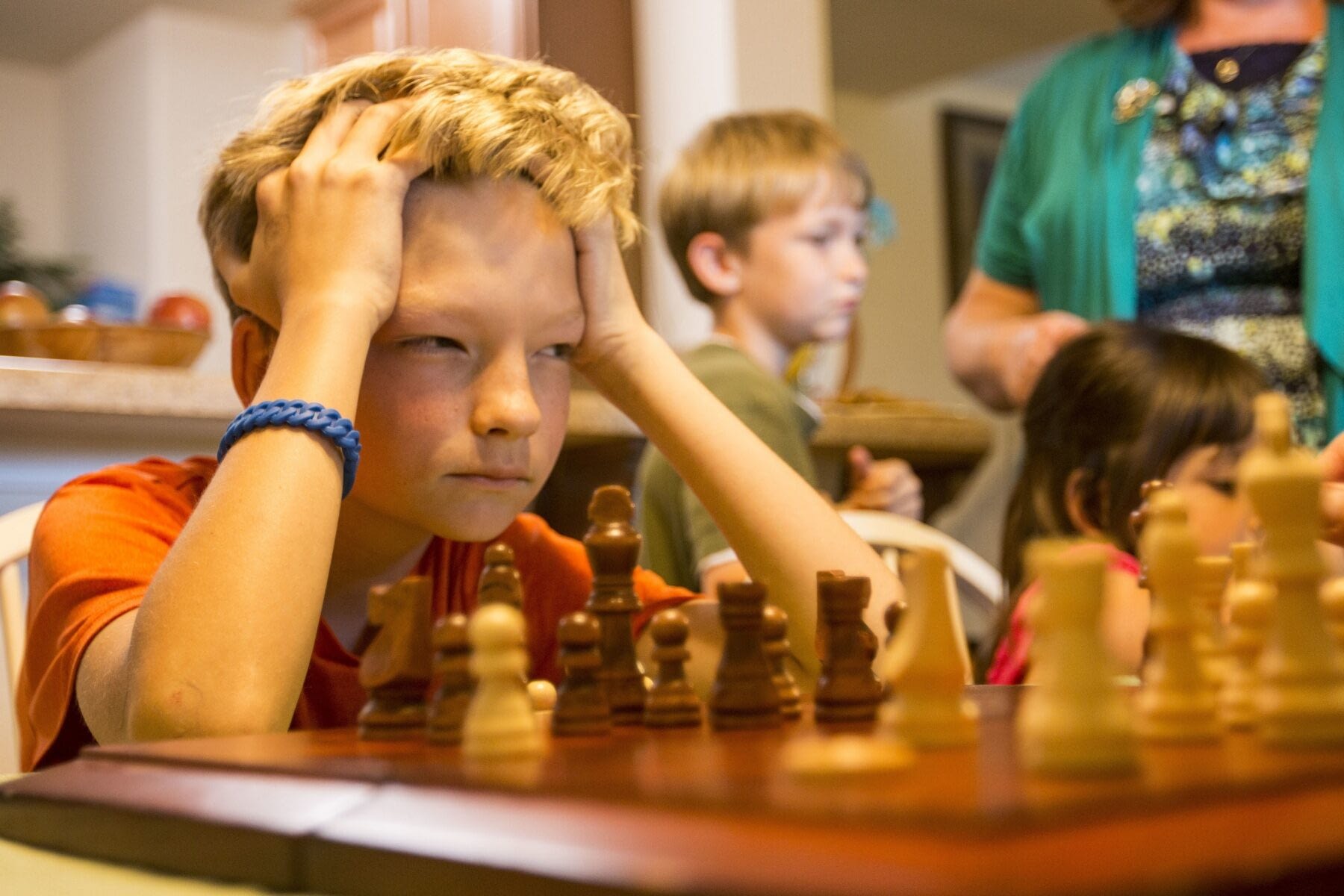 Image: young chess champion concentrates intently on a game of chess with his head resting on his hands